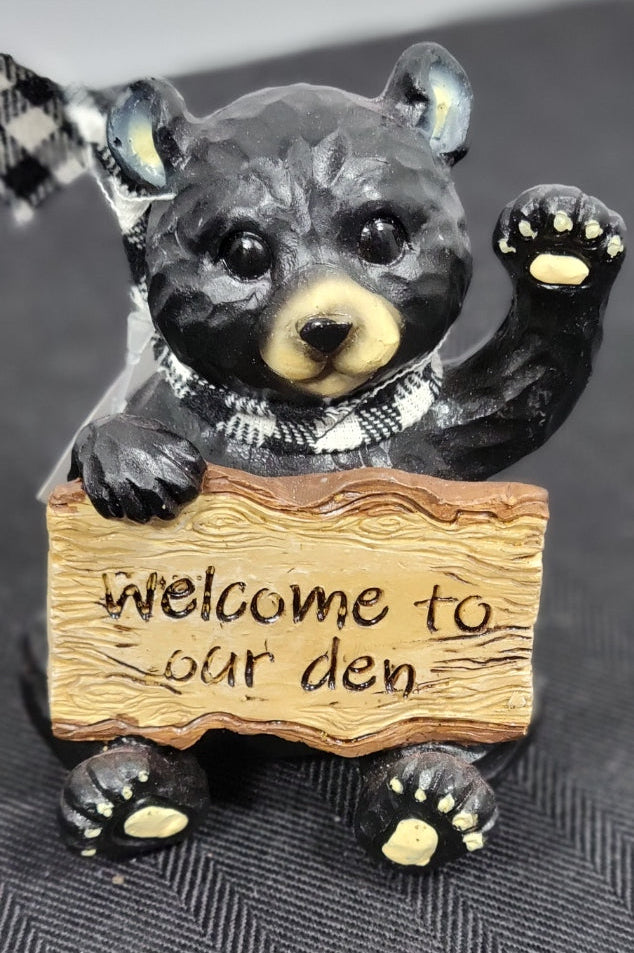 Bear figurine holding a 'Welcome to our den' sign on a dark background