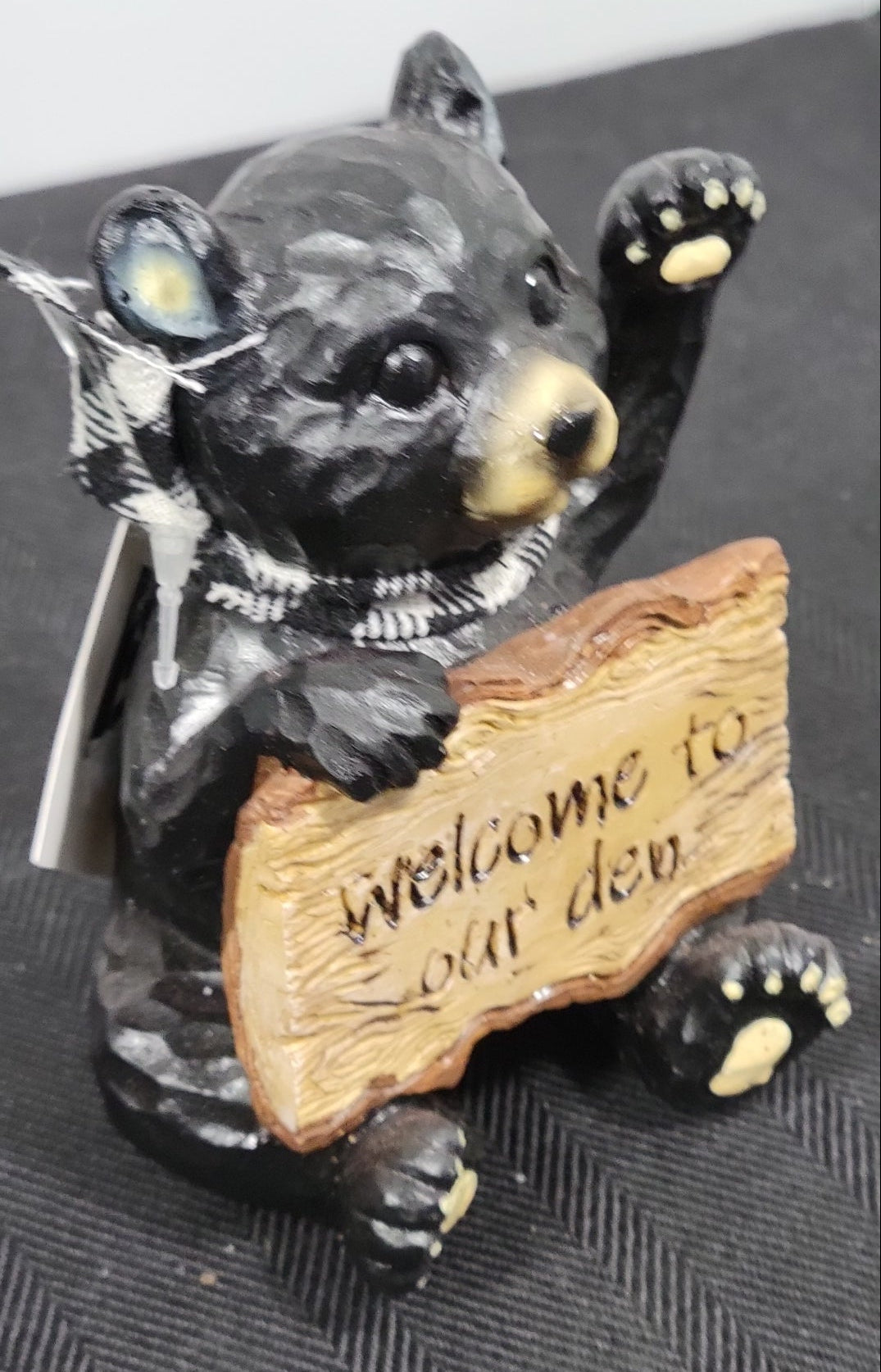 Black bear figurine holding a wooden sign on a textured surface