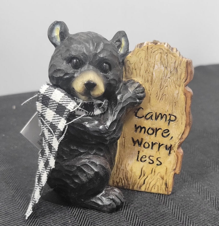 Bear figurine holding a sign with 'Camp more, Worry less' text on a textured surface.