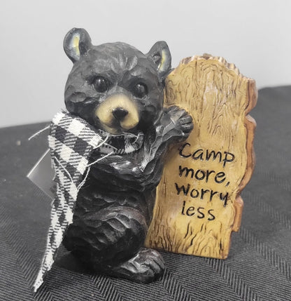 Bear figurine holding a sign with 'Camp more, Worry less' text on a textured surface.