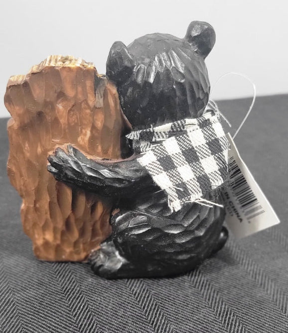 Black bear figurine with a checkered towel over its shoulder on a gray surface.